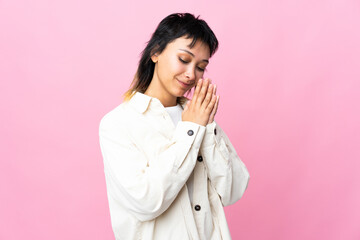 Young Uruguayan woman over isolated pink background keeps palm together. Person asks for something