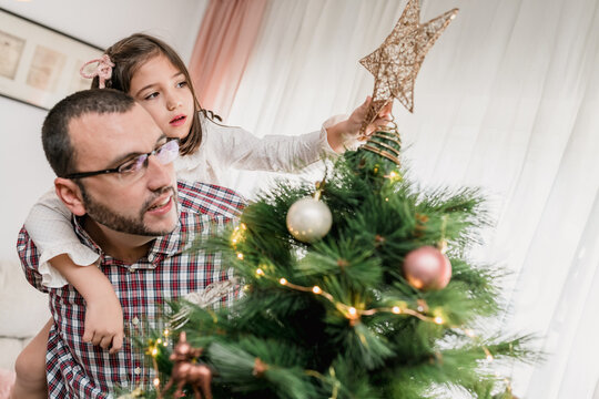 Father and daughter decorating Christmas tree with star