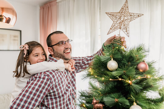 Father and daughter decorating Christmas tree with star