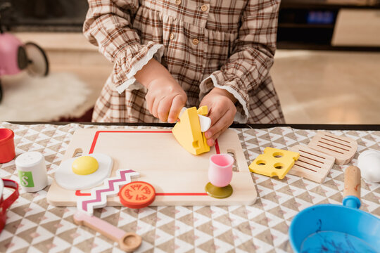 Crop girl cutting toy cheese while cooking at home