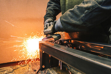 A factory worker is cleaning a metal part with an industrial grinder. A worker works in production. 