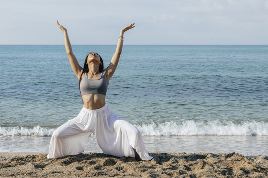 Asian woman doing Goddess with Arms Up pose on shore