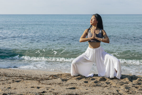 Contemplative ethnic woman doing Goddess pose on ocean coast