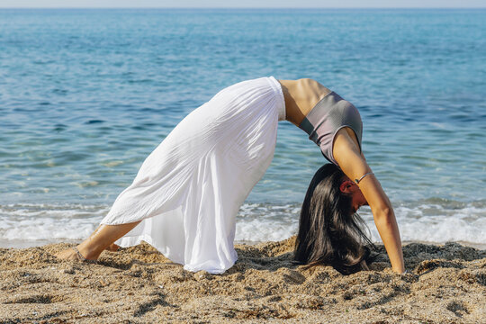 Flexible woman doing Wheel pose on sea shore