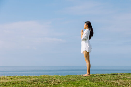 Asian woman with praying hands meditating on sea shore