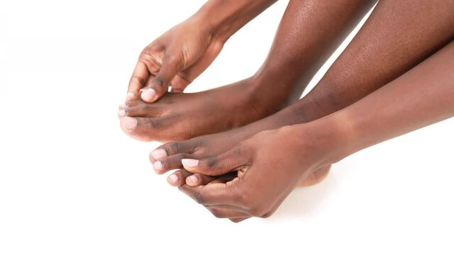 Close up of an African woman's hands massaging her toes and feet. Isolated on a white background.