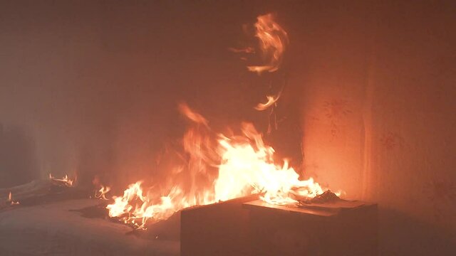 The bedroom is on fire with a lot of smoke. The bed, bedside table, plastic teapot, wallpaper and bookshelves are in flames in a residential home. Cinematic shot of aftermath of a two alarm fire 4k
