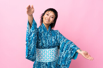 Young woman wearing kimono over isolated blue background presenting and inviting to come with hand
