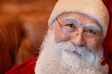 Portrait of smiling kind senior Santa Claus with white beard and eyebrows wearing eyeglasses and cap