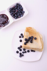 Crepes, thin pancakes with blueberry jam and fresh berries on white background. Fresh and tasty morning sweet brackfast. Flat aly