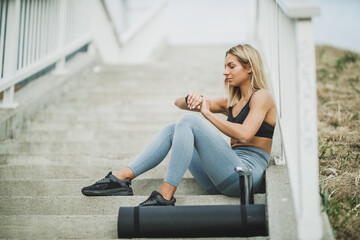 Fototapeta na wymiar Woman Looking On Smartwatch While Sitting On The Stairs Before Outdoor Working Out