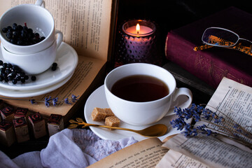 old books, tea, glasses candle on a dark table