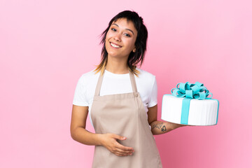 Uruguayan Pastry chef holding a big cake over isolated pink background holding copyspace imaginary on the palm