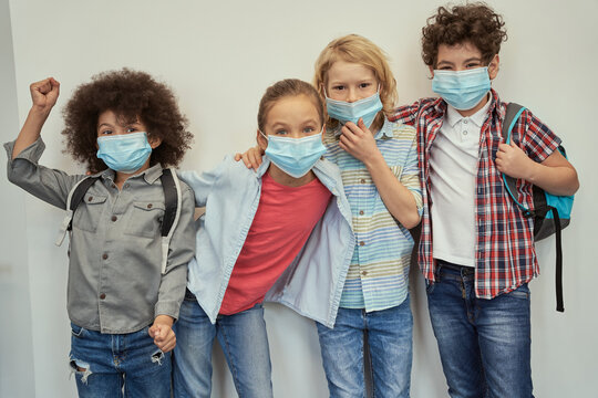 Enthusiastic Pupils. Charming Diverse Kids Wearing Protective Face Masks Looking At Camera, Posing Together Over Light Background