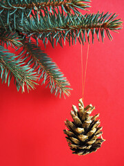 a cone, painted in gold, hangs on the branches of a blue Christmas tree on a red background. side view