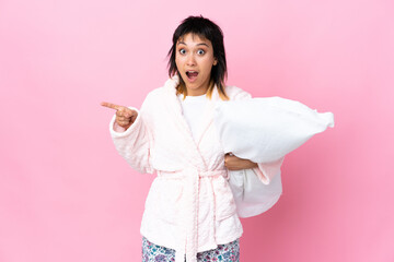 Young Uruguayan woman in pajamas over isolated pink background surprised and pointing finger to the side