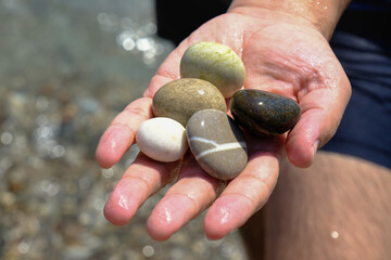 Smooth pebbles of different colors in the palm.Sea ​​background