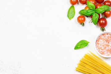 Raw spaghetti, Himalaya salt, cherry tomatoes and fresh aromatic basil on white marble background with copy space for your design. Food blog template. Recipe book cover mock up.