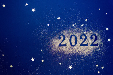 Numbers 2022 on dark blue background are decorated with sparkles and star confetti. New Years celebration concept. Copy space