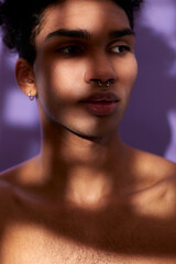 Verticale portrait of sensual young man in shadows. Sensitive hispanic model on purple background