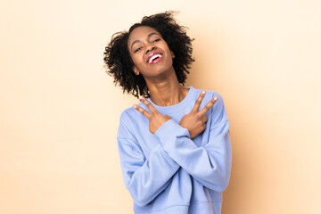 Fototapeta premium Young African American woman isolated on beige background smiling and showing victory sign