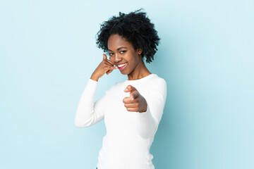 Young African American woman isolated on blue background making phone gesture and pointing front