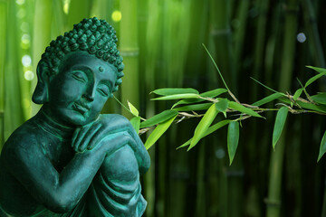 Sitting Buddha figurine mediating, situated in a sunny garden and surrounded by bamboo leaves