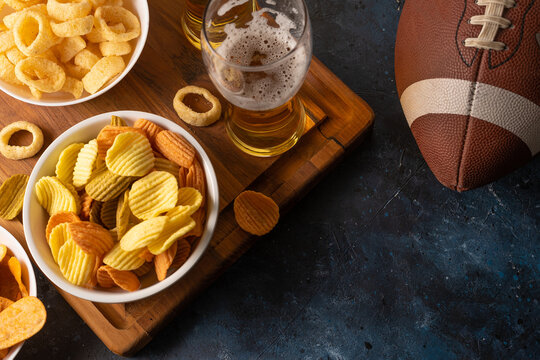 Light beer in glasses, potato chips, onion rings on a wooden tray. Baseball glove. High angle view. Watching sports matches and your favorite TV shows. Rest with friends.
