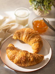 Traditional French breakfast - two croissants on a white earthenware plate, orange jam and milk. White silk tablecloth. Beautiful composition. Restaurant, hotel, bakery, menu design.
