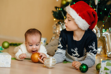 Fototapeta premium A little boy and his brother play with gifts under a festive Christmas tree. Happy Christmas and New Year celebrations
