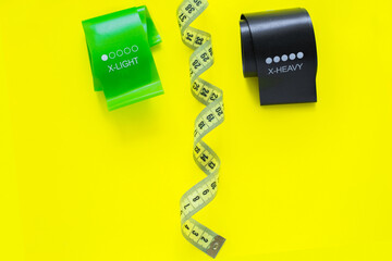 Two fitness tapes of black and green color are located at the top of the photo on a yellow background, they are separated by a yellow measuring tape. top view, flat lay, copy space, isolate