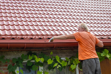 A man cleans out debris and leaves from the gutter system on the roof of his house © Natalia
