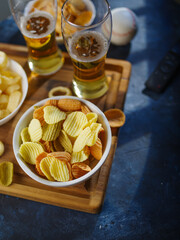 Two glasses of light beer, potato chips, onion snacks and a TV remote on a blue background. Low angle view. Watching your favorite TV shows with friends, with your family, beer, cold snacks.