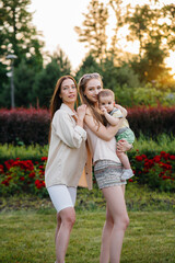 Fototapeta premium A young homosexual family of mothers hugs and plays in the park with their young son during sunset. Modern happy lesbian family.