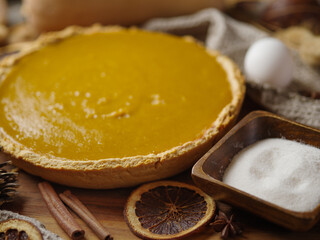 American Pumpkin Pie and Ingredients - 2 cinnamon sticks, sugar, eggs, a circle of citrus. Beautiful composition. Macro photography. Thanksgiving, Halloween. New Year. Christmas.