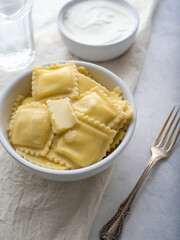 Ravioli in a white bowl. There is a fork nearby. Sour cream in a bowl in the background. White background. Low angle view. Italian food. Restaurant, hotel, home cooking. Menu design ..
