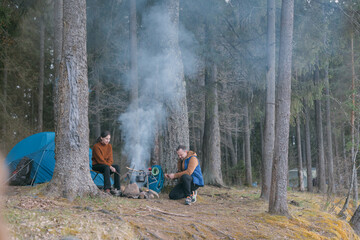 Fototapeta premium A married couple prepares food on a campfire on the shore of the lake with a tent.