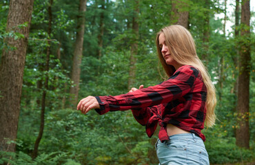 An attractive Caucasian female fastening the bottoms of her flannel shirt in the forest