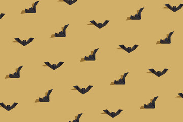 Obraz na płótnie Canvas Halloween pattern made of black paper origami bats isolated on ocher or gold background. Sun and shadows. Minimal, abstract Halloween texture. Party decoration idea. 