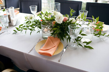 A table is served in a restaurant with a beautiful decor. The cafe hall is waiting for guests for a festive dinner. The plate is decorated with a coral towel, floating candles and flowers