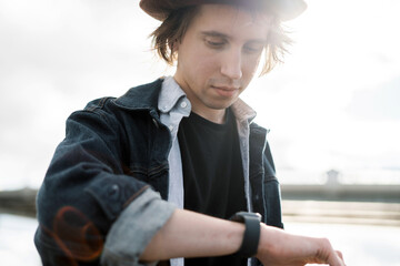 A young male hipster. A teenager responds to friends in a message on a smartwatch social network. The freelancer is stylish in a hat in the city.