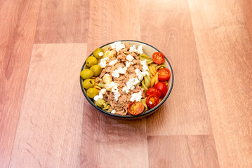 Bowl of pasta salad with fresh cheese, cherry tomatoes, green pitted olives and canned tuna.