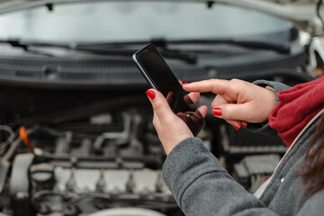 Hands of a young latina using her cell phone on her broken car engine