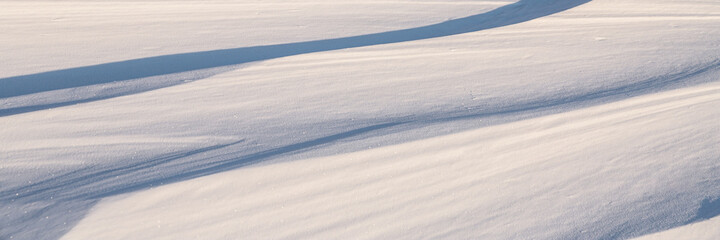 Beautiful winter background with snowy ground. Natural snow texture. Wind sculpted patterns on snow surface. Wide panoramic texture for background and design.