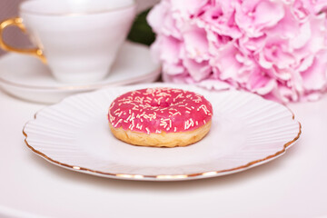 Cup of tea, sweet strawberry donut on golden plate with hydrangea flower