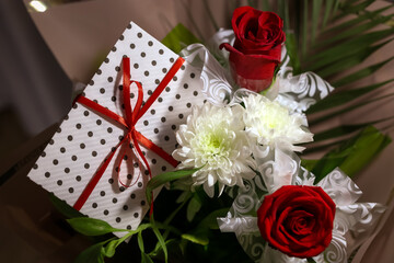3 red roses  bouquet with gift envelope, red ribbons, white paper for certificates, invitation card inside. Craft concept. Red on the red background.   Weddig, ceremony concept, holidays, surprises.