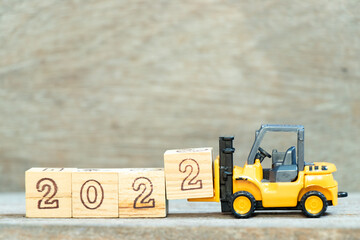 Toy forklift hold letter block 2 to complete word 2022 on wood background