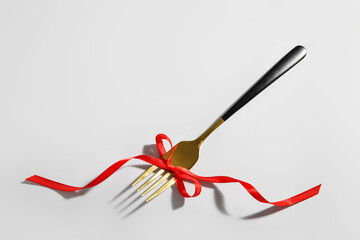 Fork with stylish ribbon on light background
