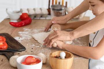 Young mother and daughter cooking together in kitchen at home