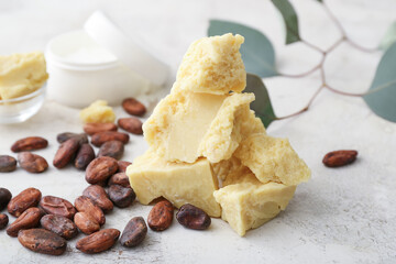 Pieces of cocoa butter and beans on light background
